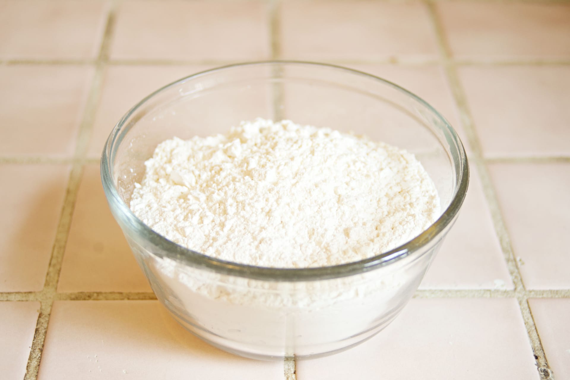 A glass bowl of fine white powder on a tiled kitchen worktop
