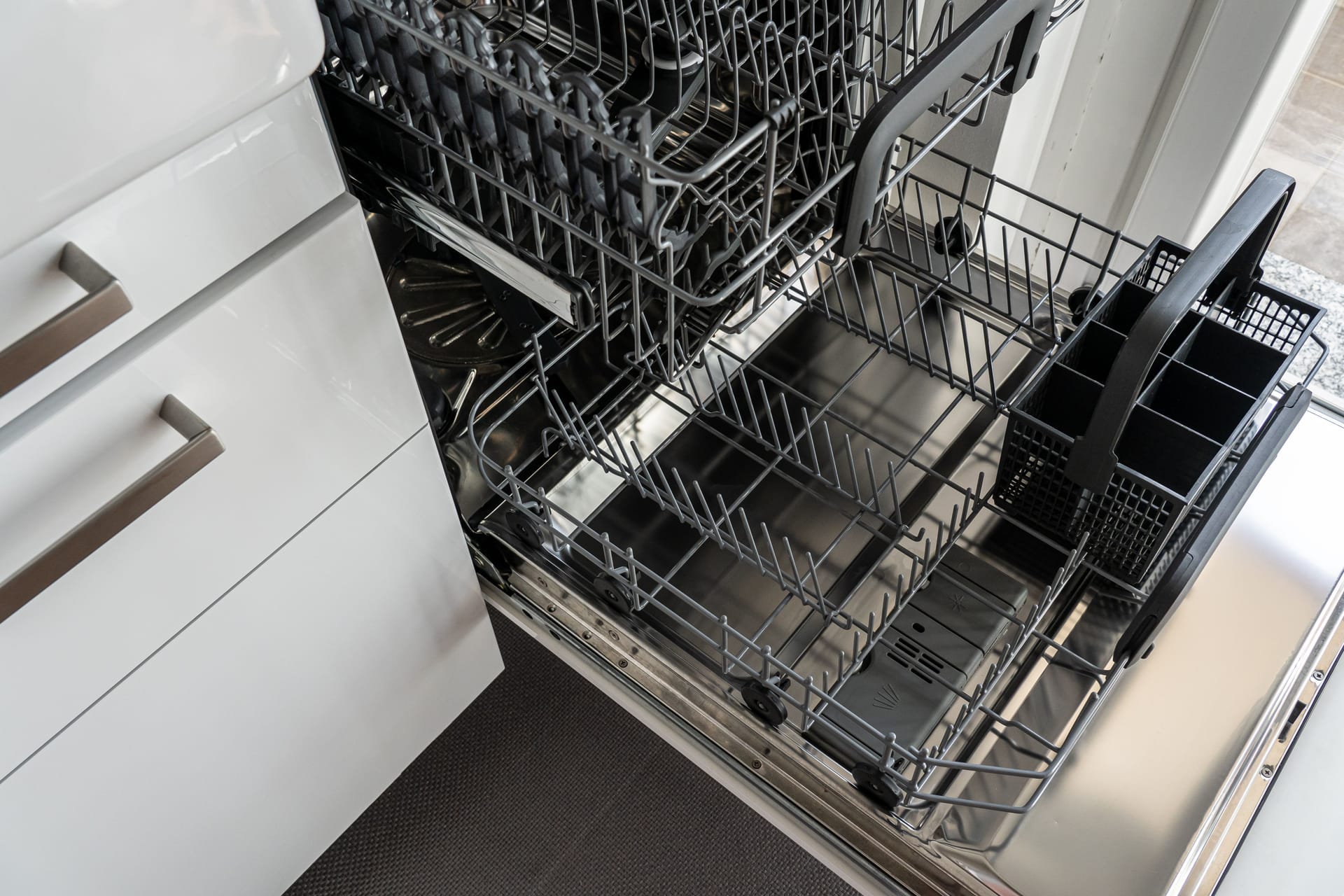 An open, empty stainless steel dishwasher in a kitchen