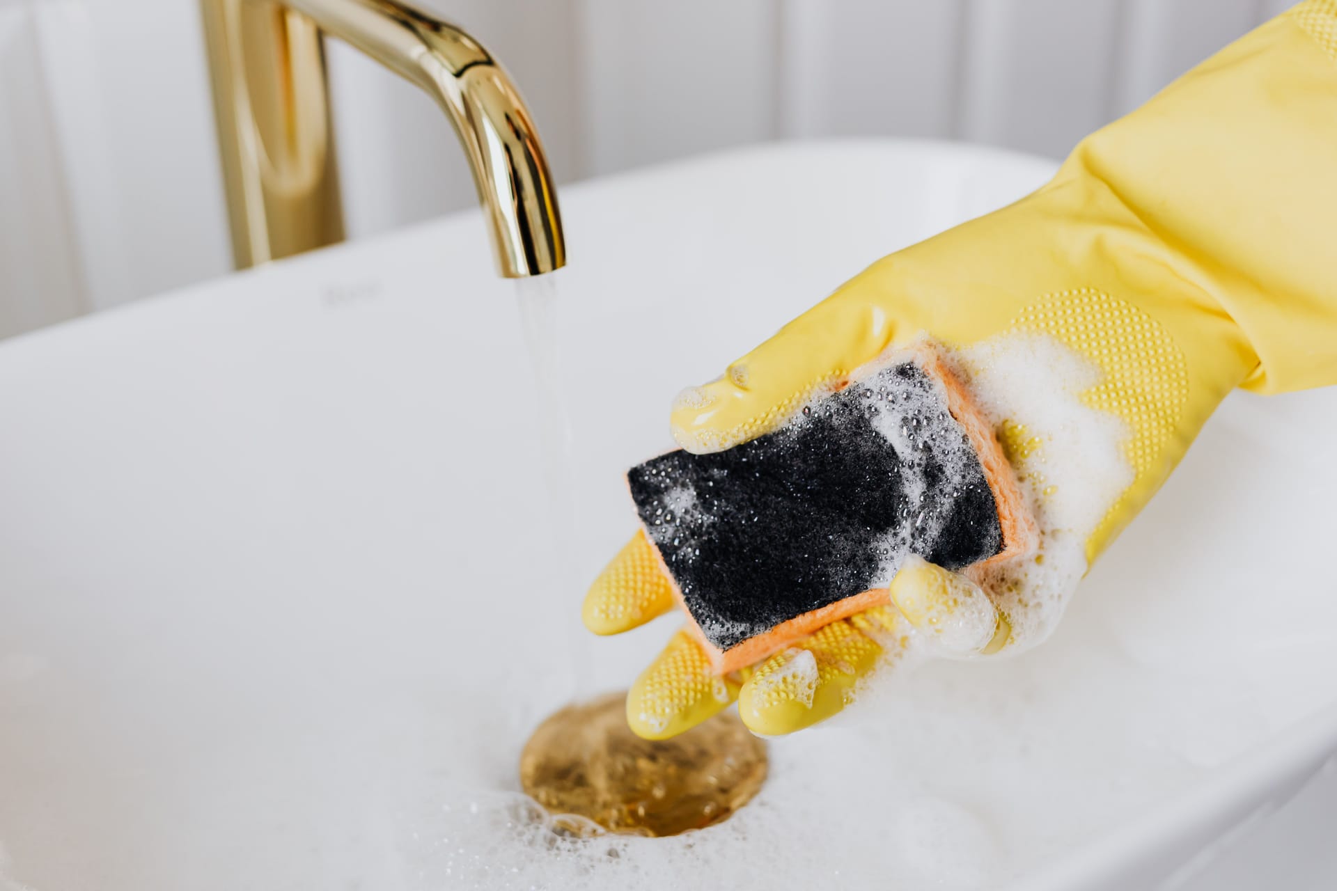 A gloved hand cleaning a white sink with a sponge