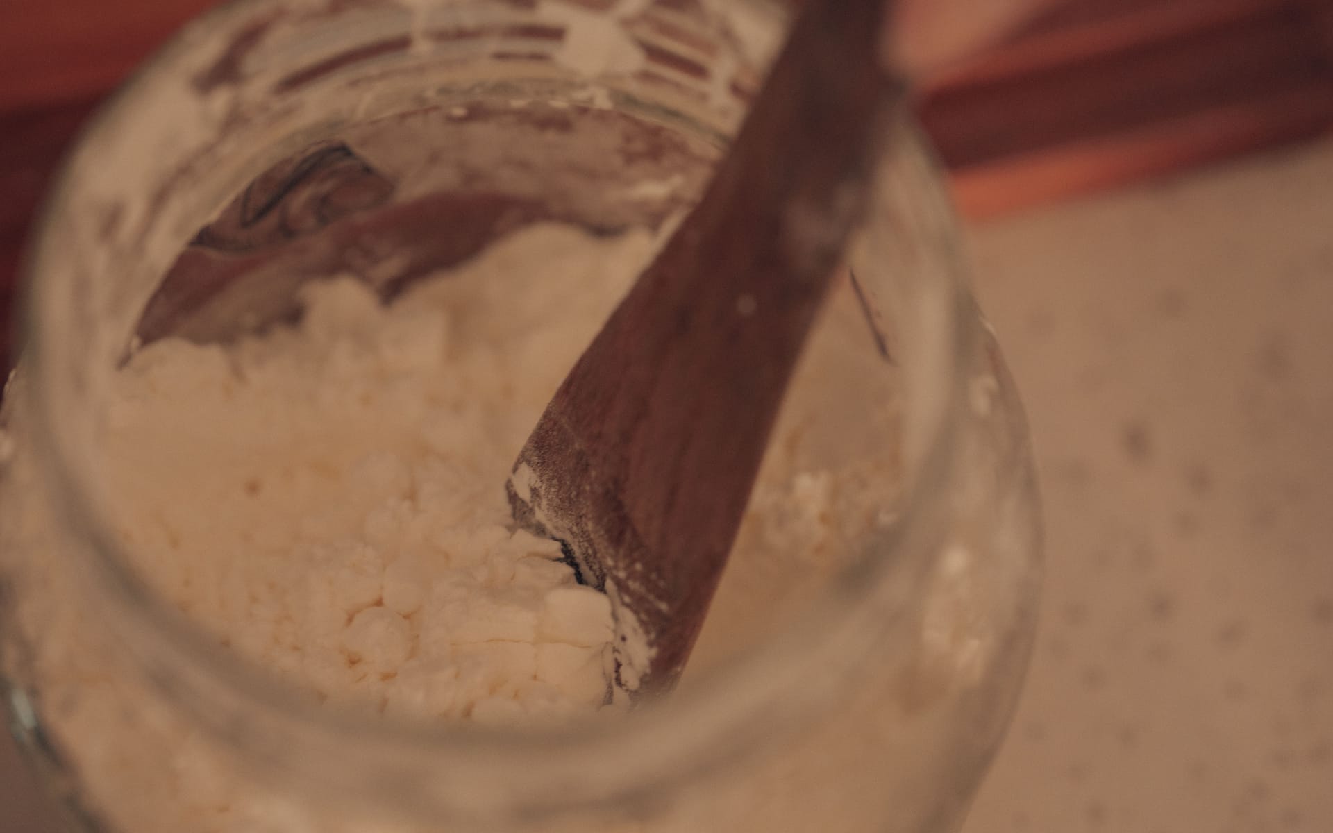 Stirring powdered ingredients in a glass jar with a wooden spoon