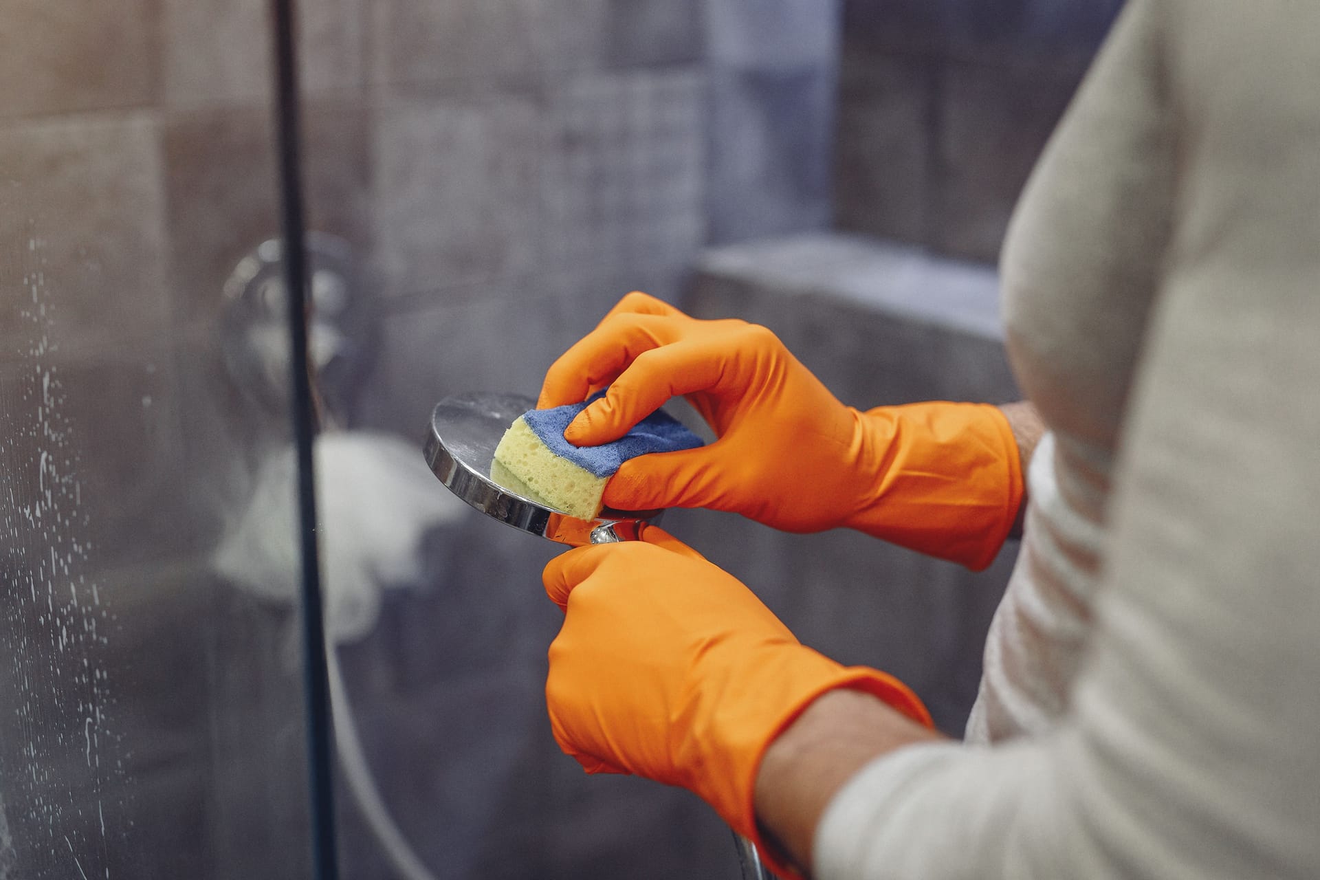 Cleaning a shower head with a sponge and rubber gloves