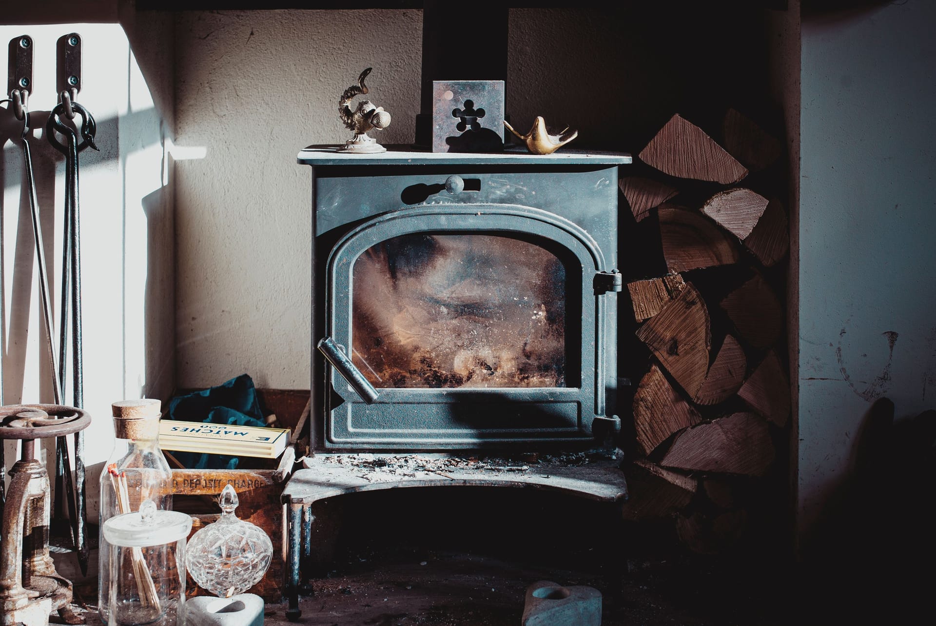 A lit wood-burning stove with a stack of split logs